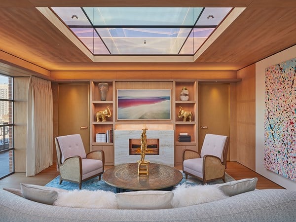 Living room of Penthouse with glass sky light, two cream armchairs and brown coffee table with gold feature on top